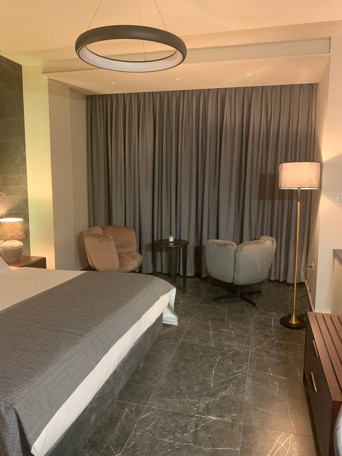 Una habitación de hotel con una cama grande, dos sillones, una lámpara de pie y una mesita con una vela.