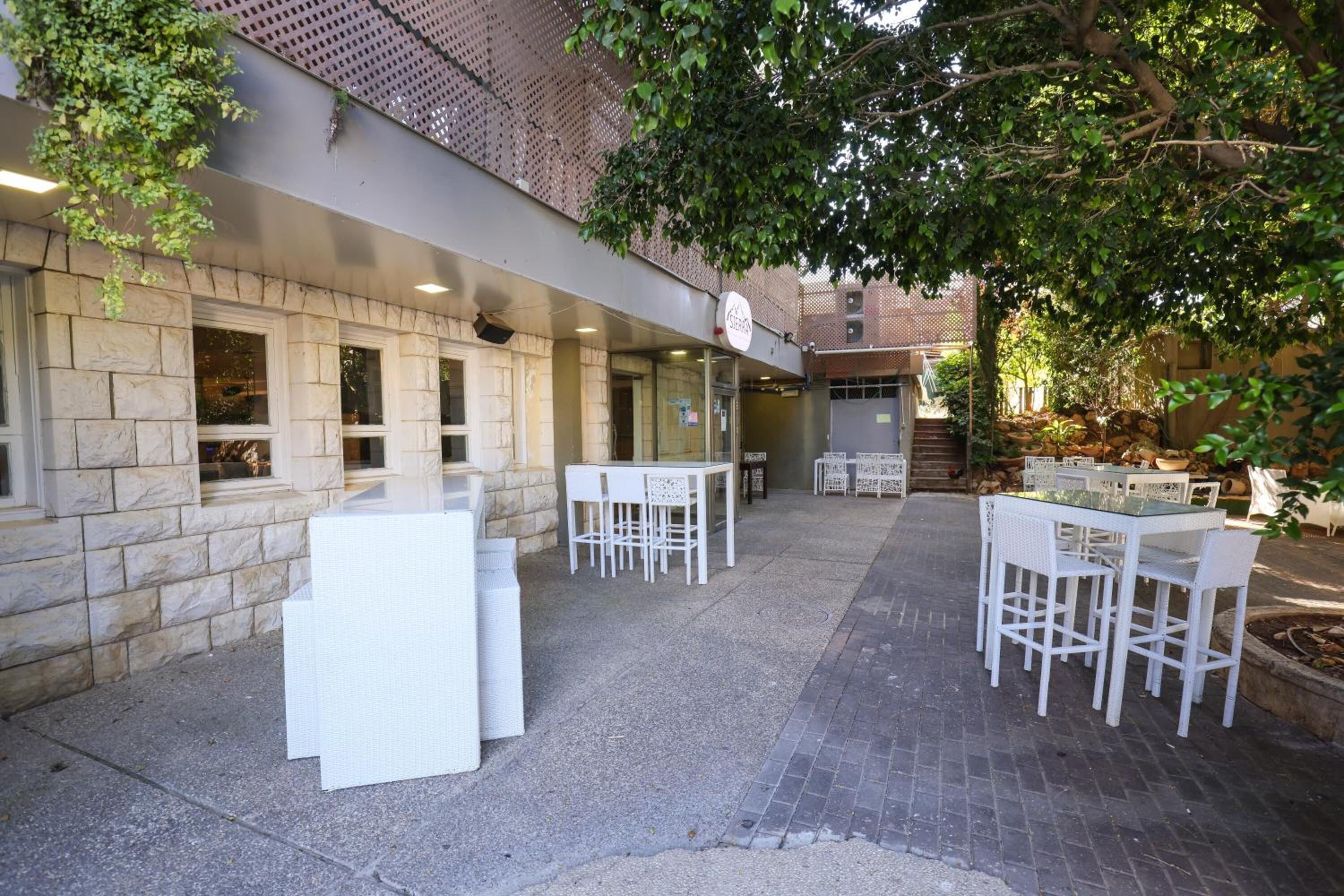 Un patio al aire libre con paredes de piedra, mobiliario blanco para exteriores y un cartel que indica un restaurante o cafetería.