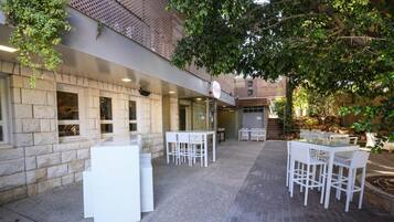 Un patio al aire libre con paredes de piedra, mobiliario blanco para exteriores y un cartel que indica un restaurante o cafetería.