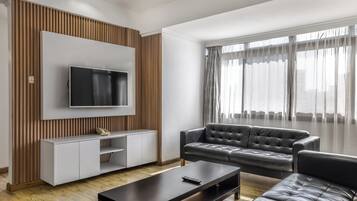 A modern living room with a flat-screen TV mounted on a white wall, a leather sofa, a coffee table, and a wooden accent wall.