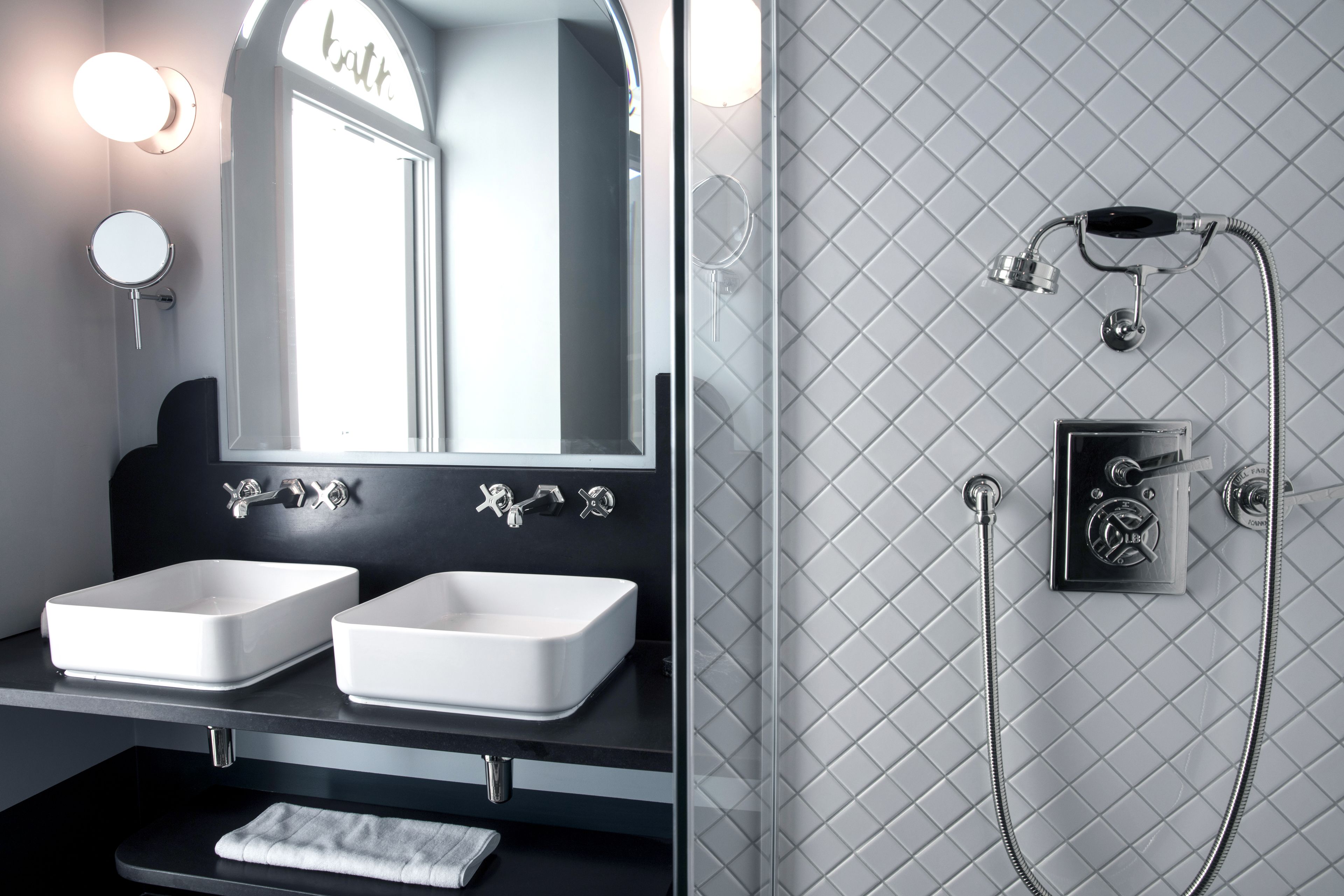 Un baño con dos lavamanos blancos, un espejo y una ducha con panel de control.