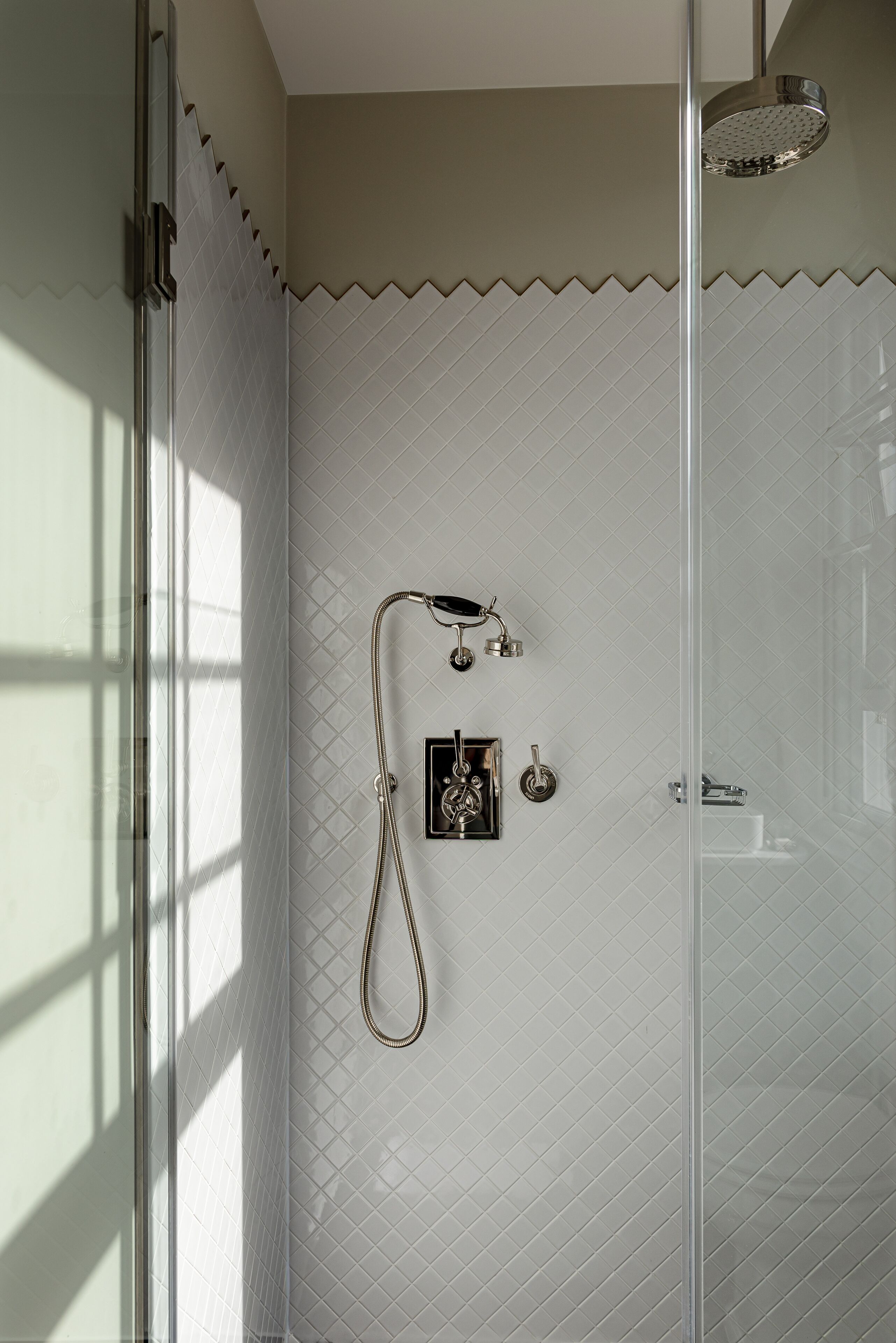 A shower area with a glass door, a handheld showerhead, and a wall-mounted faucet.