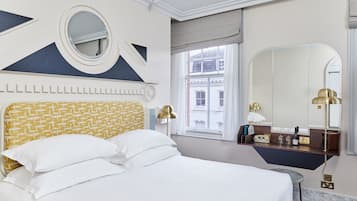 Ein Hotelzimmer mit einem Bett, einem runden Spiegel, einem Schminktisch mit Spiegel und einem Fenster mit Blick auf Gebäude.
