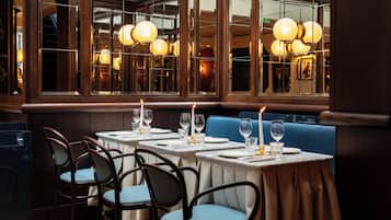 Un restaurante con mesas dispuestas para comer, sillas y un amplio ventanal con iluminación decorativa.