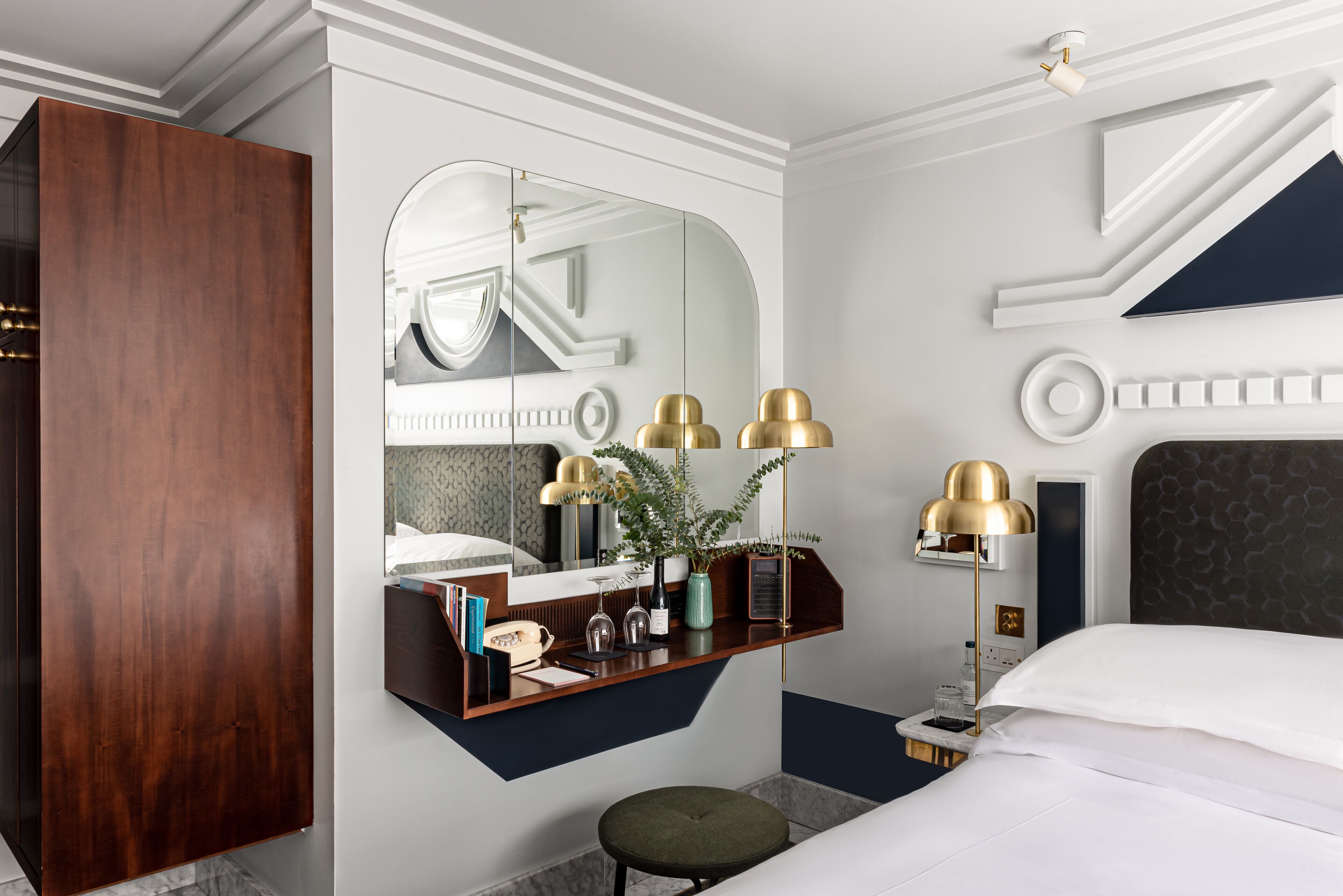 Ein modernes Hotelzimmer mit einem großen Bett, einem Schminktisch mit Spiegel und einem Schreibtisch mit Lampe.