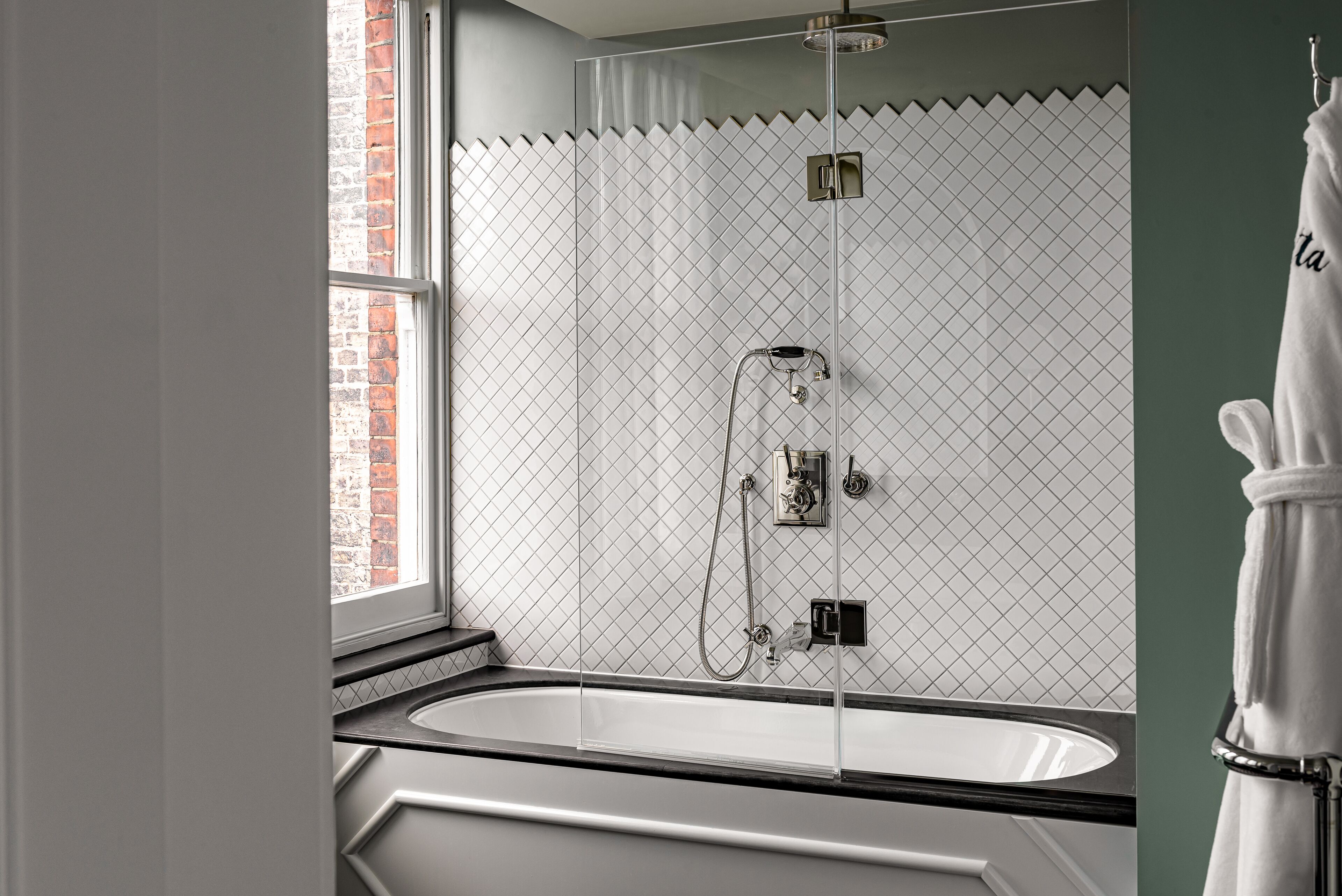 A modern bathroom with a freestanding bathtub, a glass-enclosed shower, and a view of a brick wall through a window.