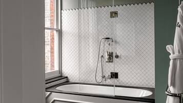 A modern bathroom with a freestanding bathtub, a glass-enclosed shower, and a view of a brick wall through a window.