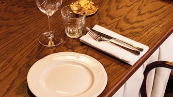 A wooden dining table with white plates, clear wine glasses, and a lit candle.