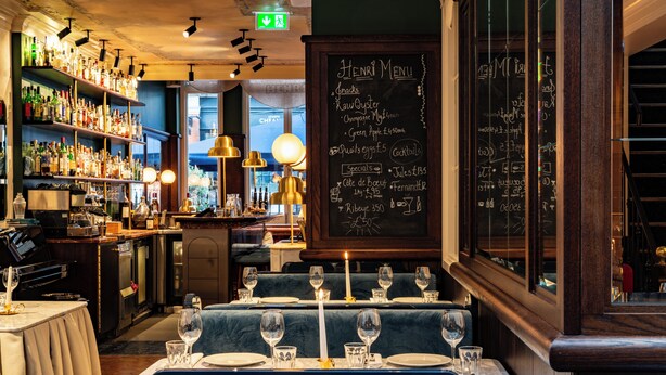 Un restaurante con un menú en pizarra, mesas dispuestas con copas de vino y estantes llenos de botellas.
