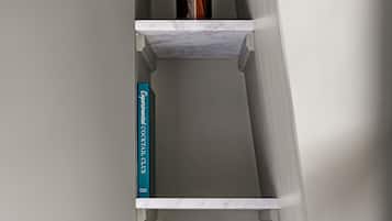 A corner shelf with a vase of dried flowers, a book titled 'Experimental Cocktails Club', and a stack of books.