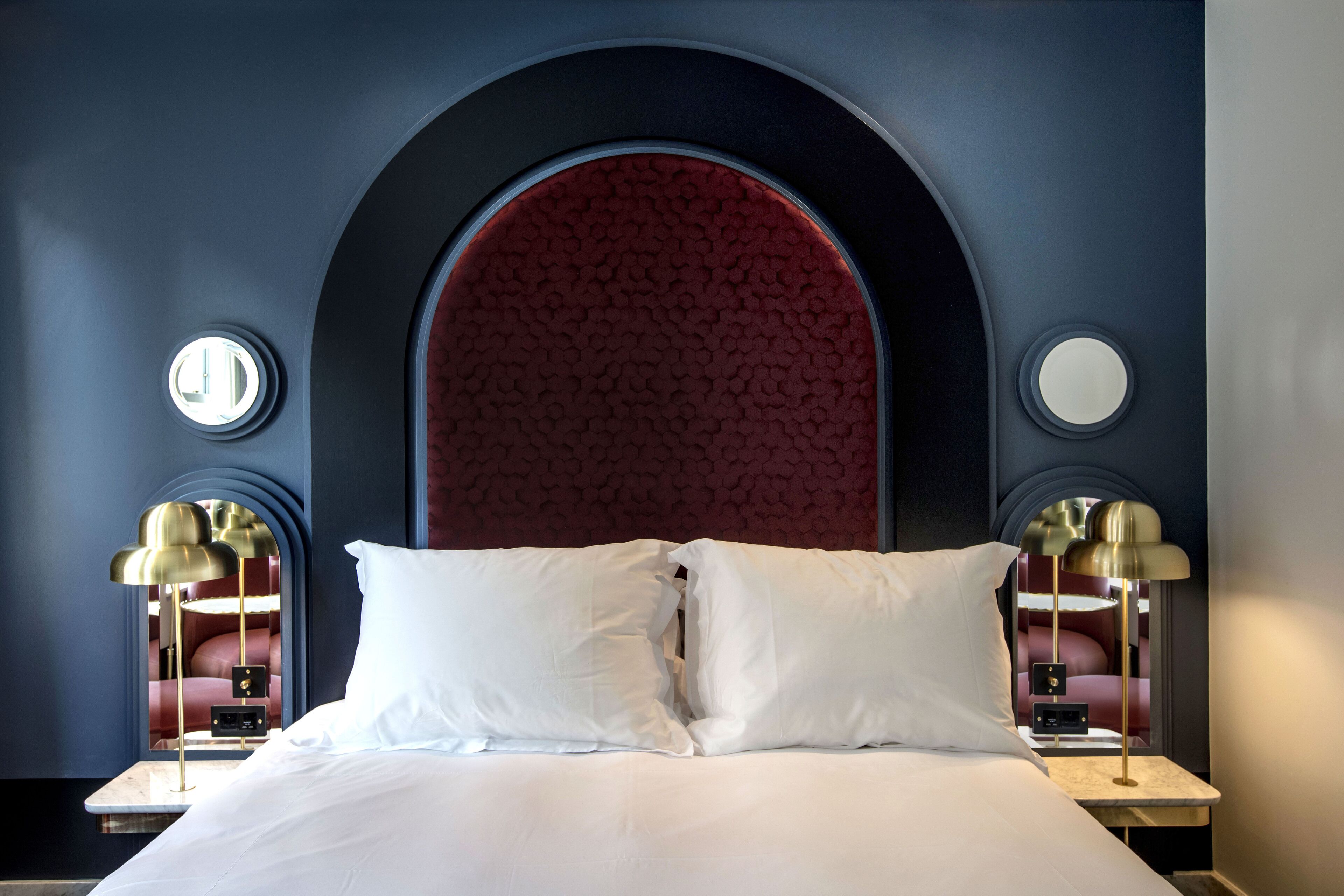 A hotel room with a large bed, two bedside tables with lamps, and a distinctive arched red headboard.