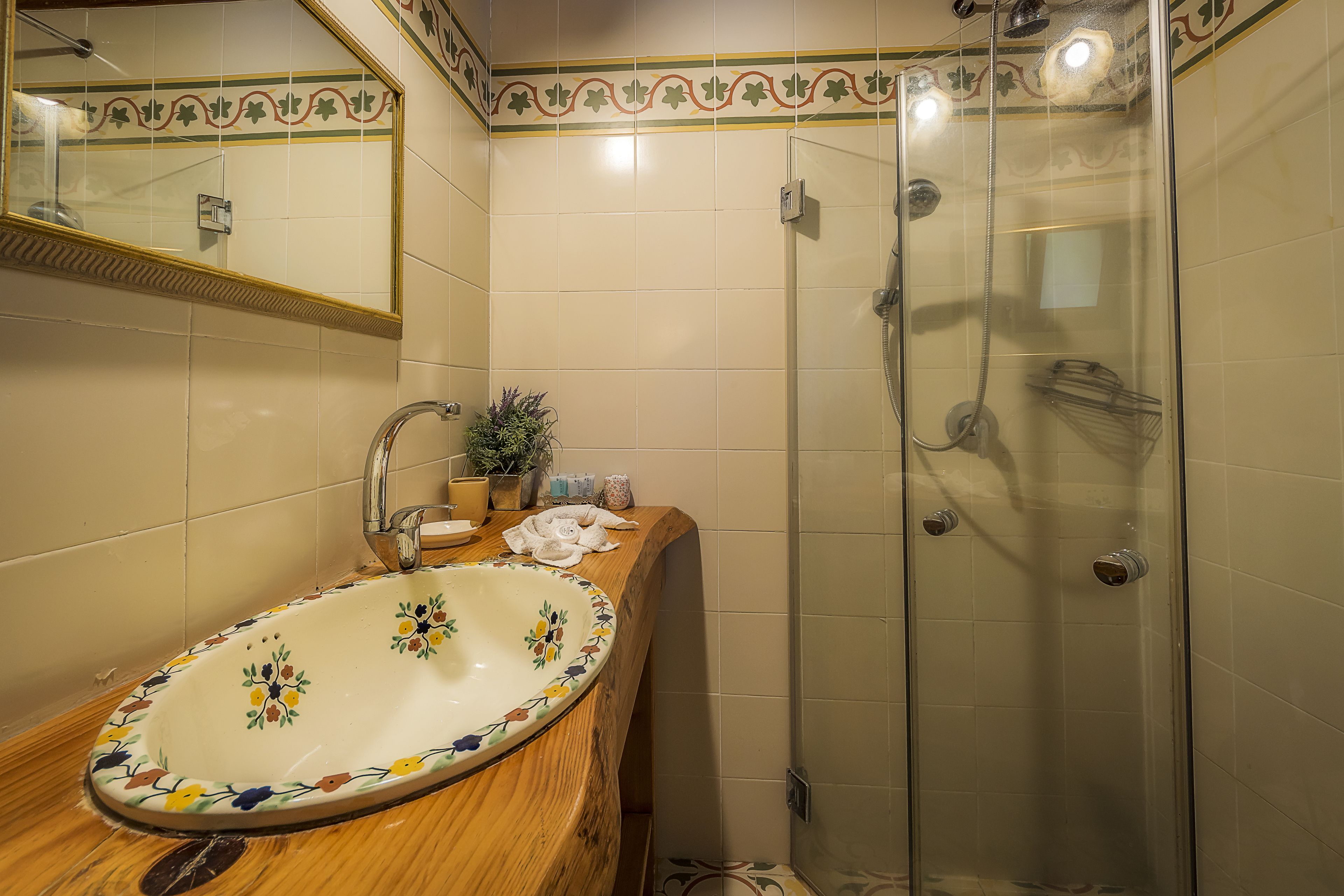 Une salle de bain avec un meuble-lavabo en bois, un lavabo décoratif, une cabine de douche en verre et un miroir orné d’un cadre décoratif.