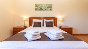 Una cama bien tendida con sábanas blancas y dos almohadas, flanqueada por dos mesitas de noche con lámparas, en una habitación de diseño sencillo y limpio.