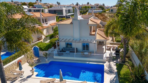 Una villa moderna con piscina, zona de estar exterior y vistas a casas vecinas.