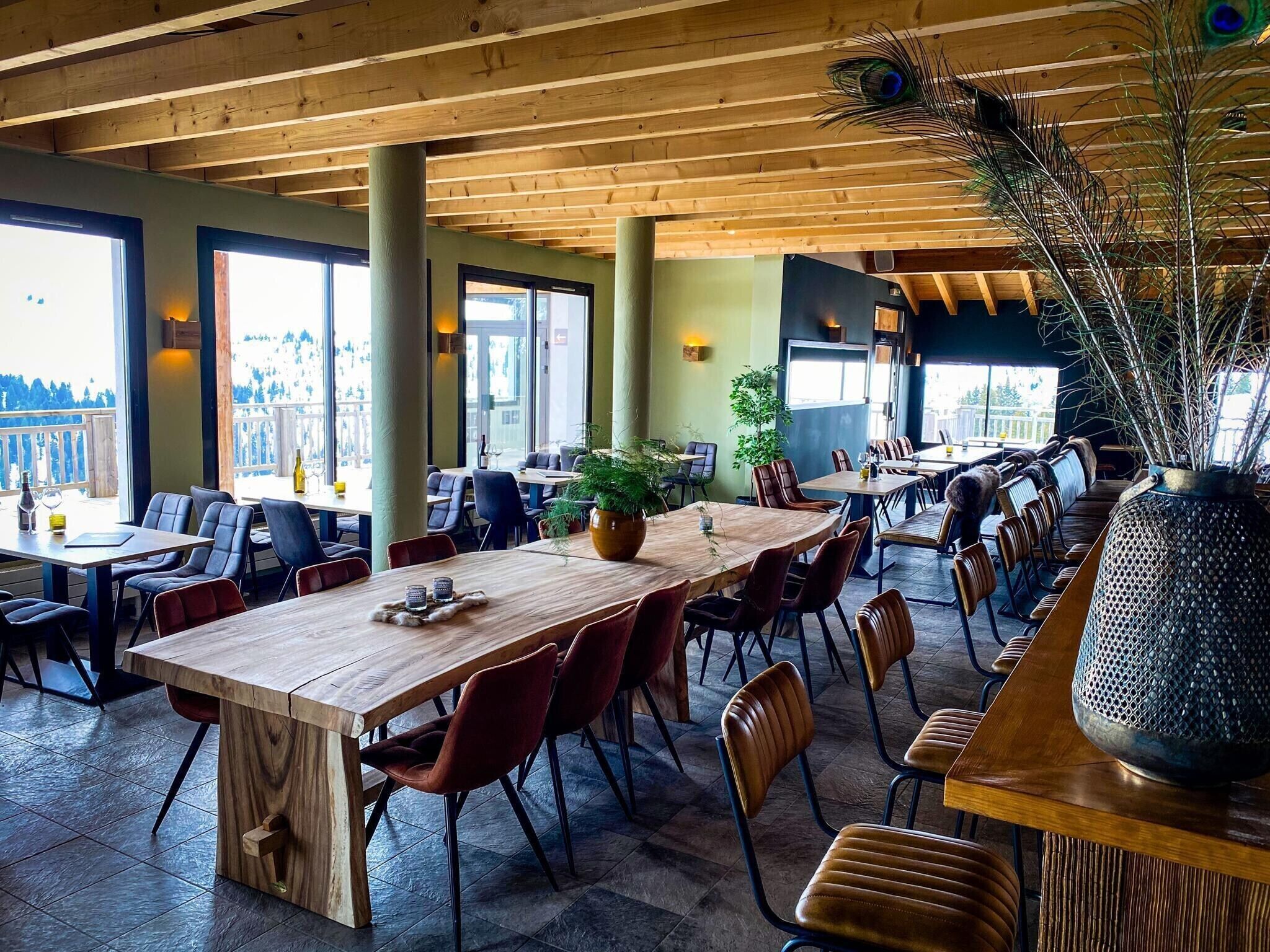 A restaurant with wooden tables and chairs, large windows, and a peacock feather decoration.