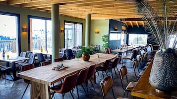 A restaurant with wooden tables and chairs, large windows, and a peacock feather decoration.