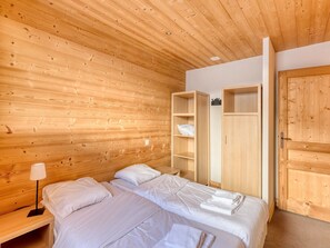 Quarto com painéis de madeira, duas camas, uma mesa de cabeceira e um guarda-roupa.