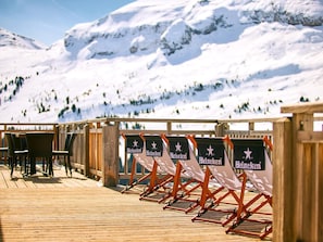 A wooden deck with seating and Heineken banners, overlooking a snowy mountain landscape.
