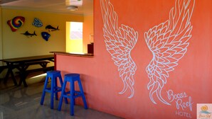 A hotel interior with a large orange wall featuring a white wing design, a wooden table, and blue stools.