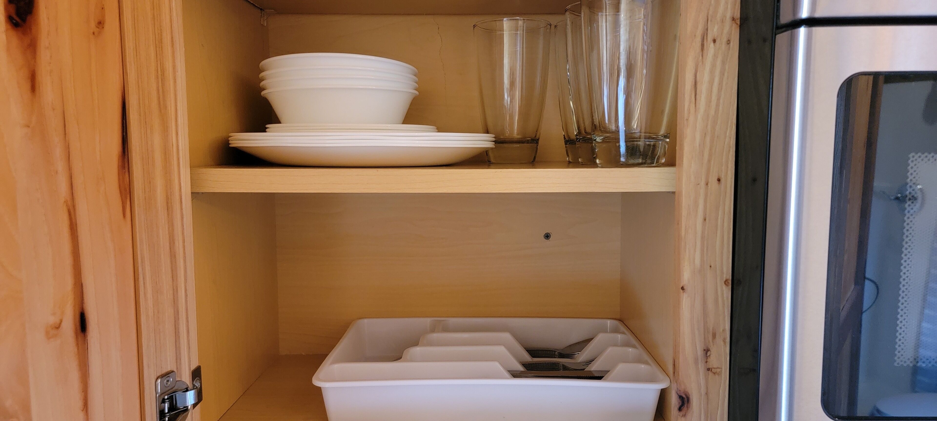 Un mueble de madera con platos blancos apilados y vasos de vidrio.
