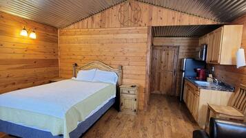 A wooden cabin room with a bed, a small kitchenette, and a wooden chair.