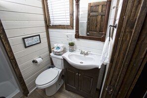 A bathroom with a white toilet, a wooden cabinet with a sink, and a framed picture on the wall.