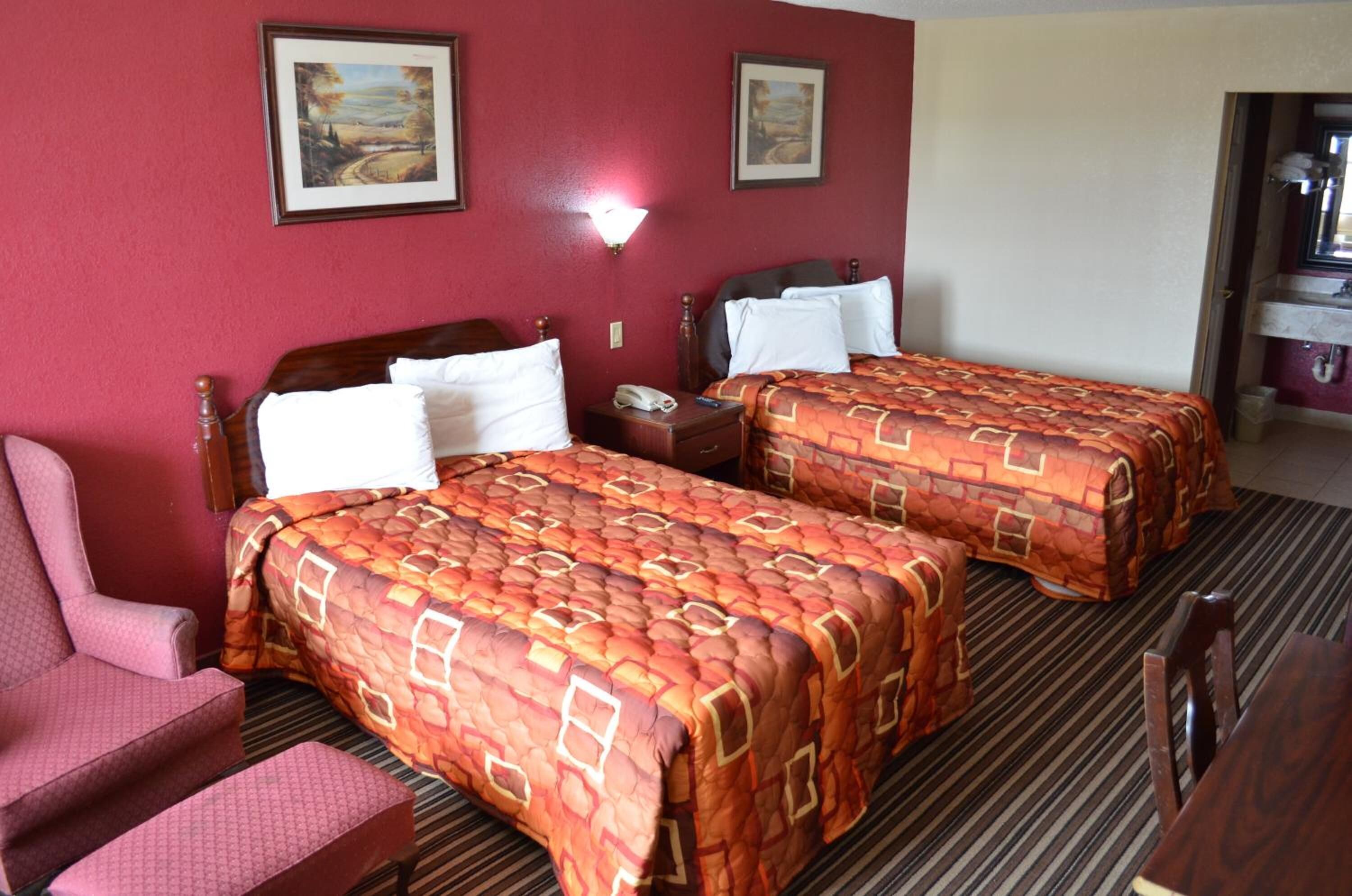 A hotel room with two beds, a chair, a bedside table, and a lamp.