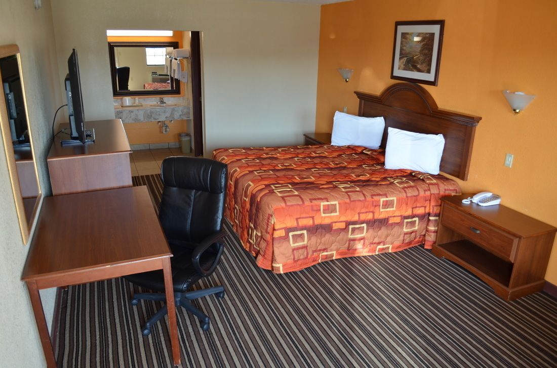 A hotel room with a bed, a desk, a chair, a telephone, and a mirror.