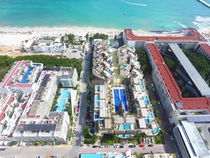 An aerial view of a coastal hotel with multiple buildings, a beach, and a clear blue sea.