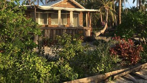 A wooden house with a thatched roof surrounded by lush greenery and tall palm trees. - Teukava Beach Oasis (Ha'atafu)