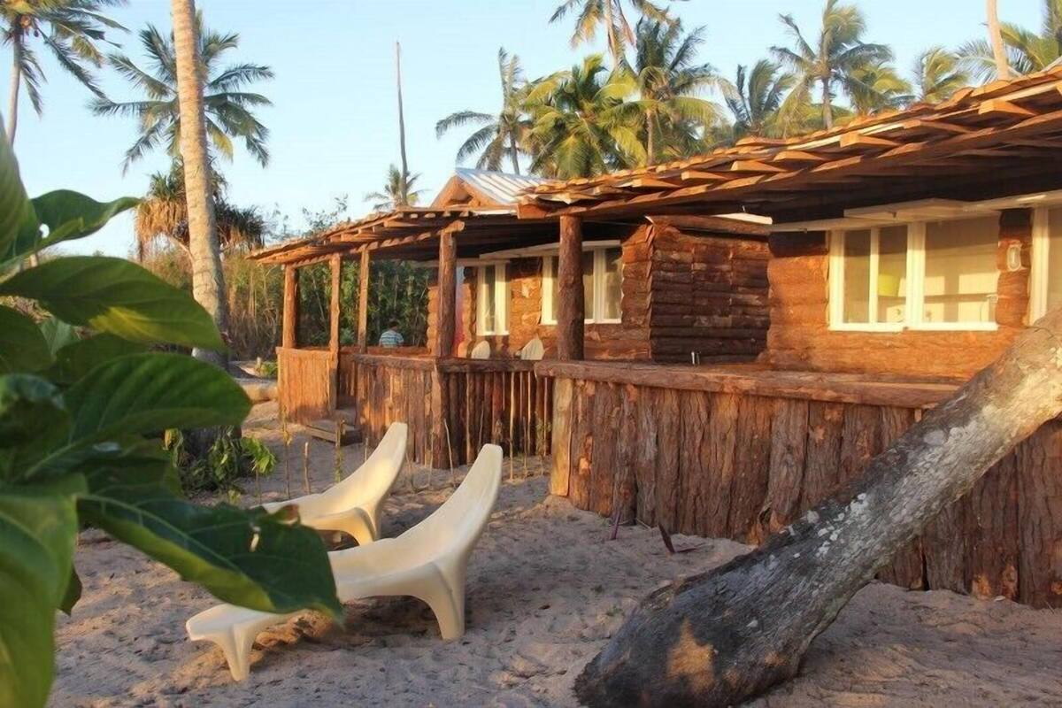 A rustic wooden building with a thatched roof, surrounded by palm trees.