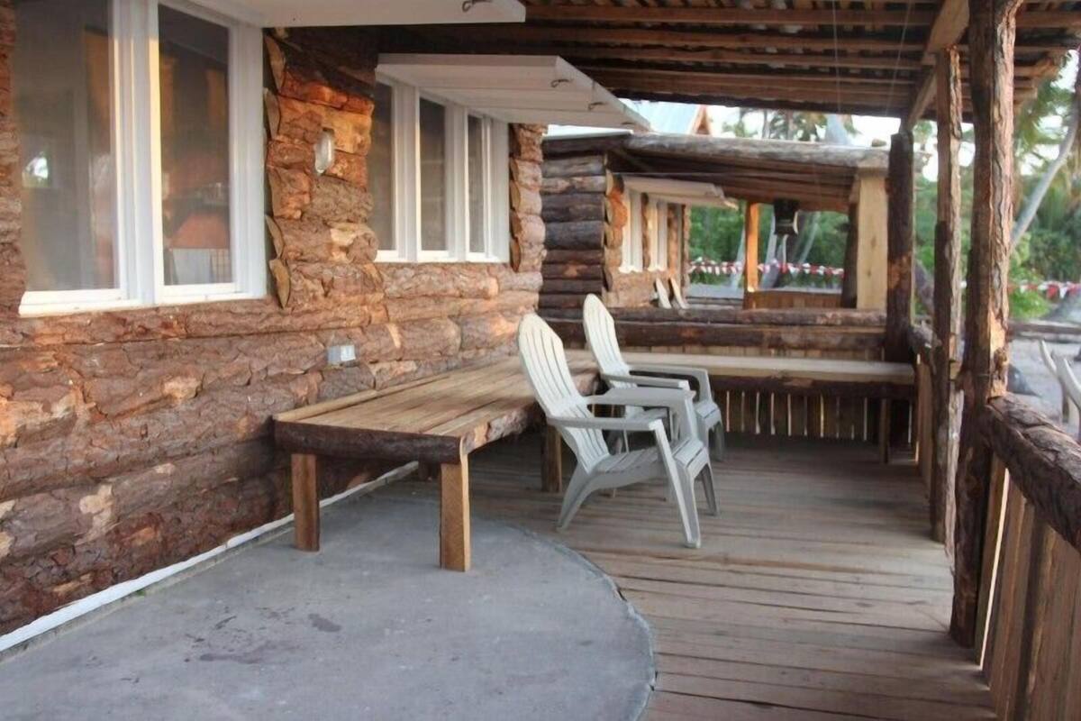 A log cabin with a wooden deck, a bench, and two Adirondack chairs.