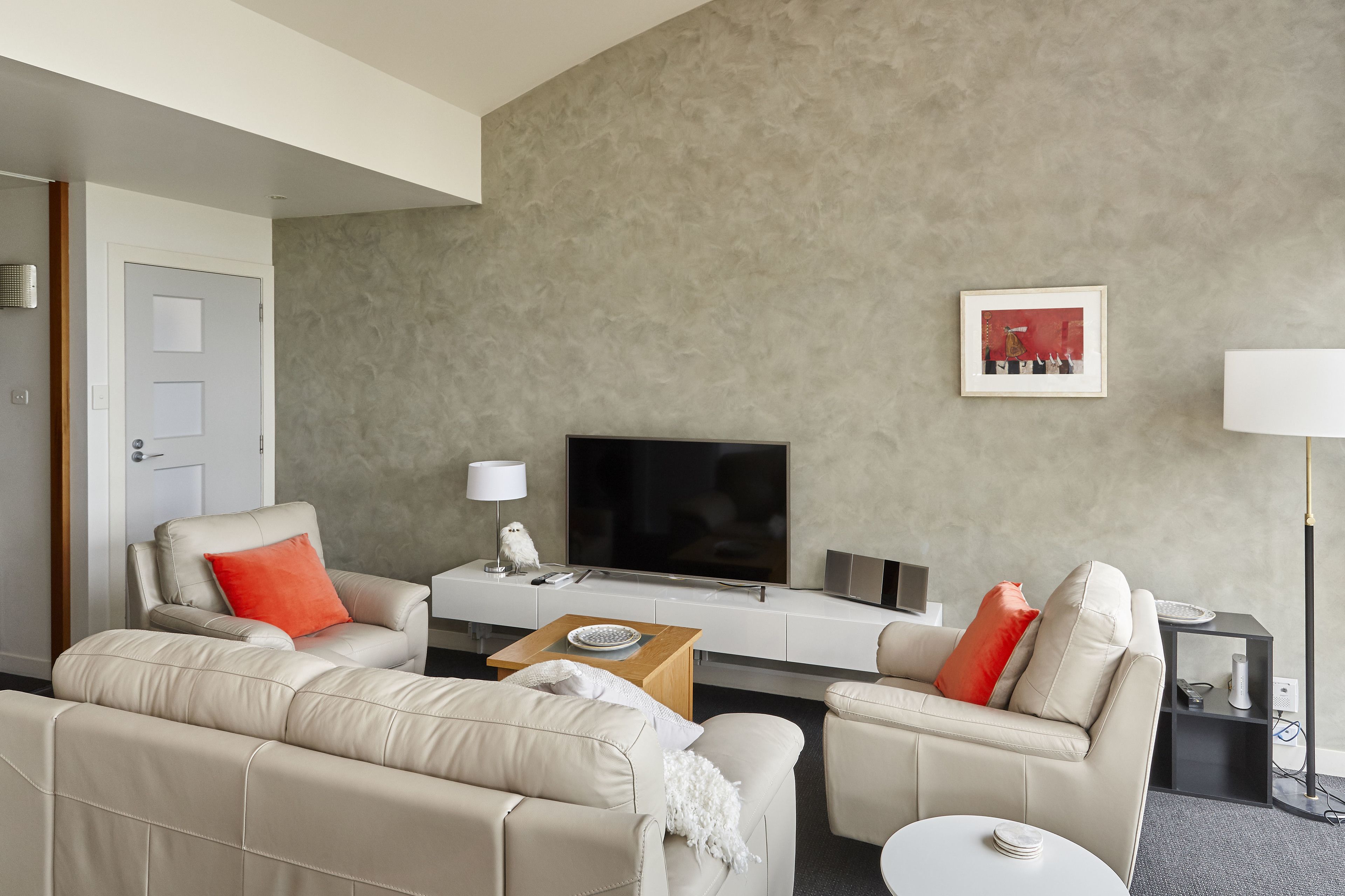 Een moderne woonkamer met een zithoek, een salontafel, een flatscreen televisie en een ingelijst schilderij aan de muur.