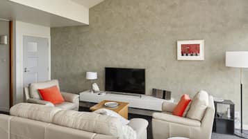 Een moderne woonkamer met een zithoek, een salontafel, een flatscreen televisie en een ingelijst schilderij aan de muur.