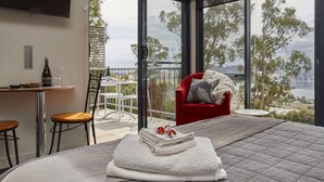 A hotel room with a bed, a dining area with a table and chairs, and a balcony with a view of the city. - Tamar River Apartments (Grindelwald)
