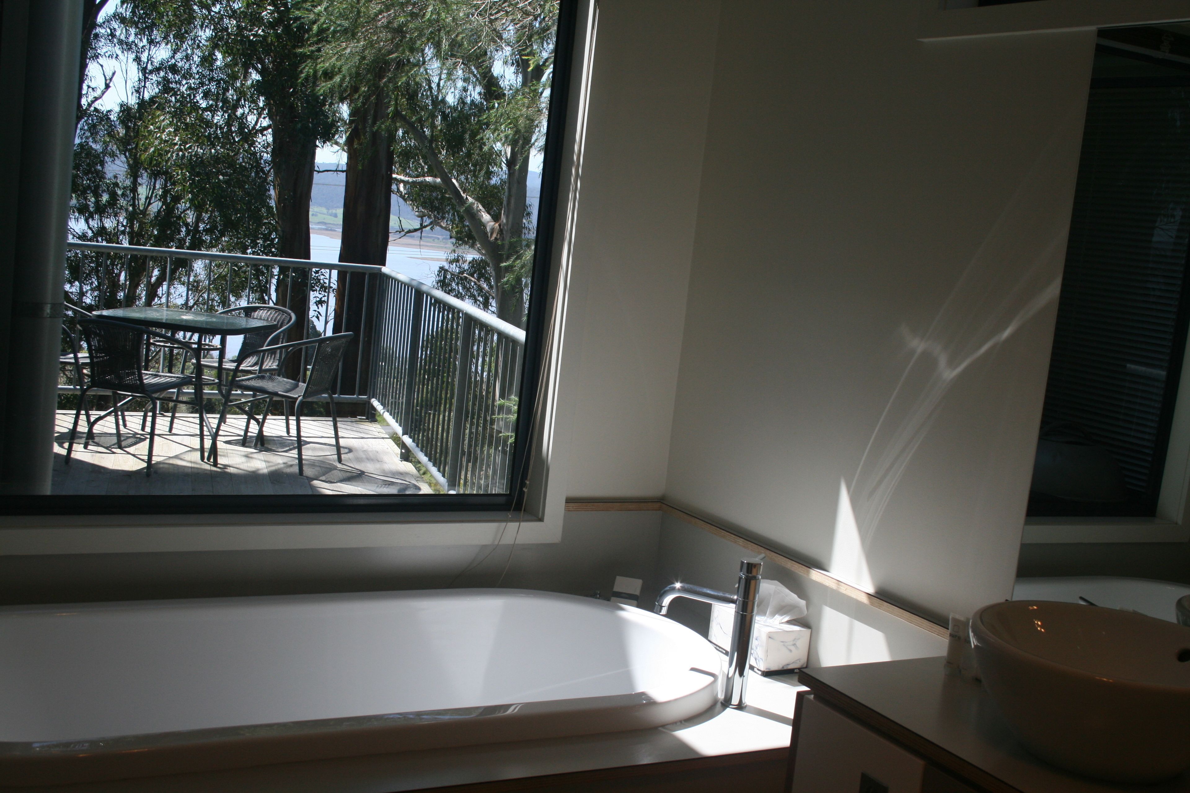 Un bany amb banyera, una finestra amb vista a un balcó amb taula i cadires, i un lavabo.