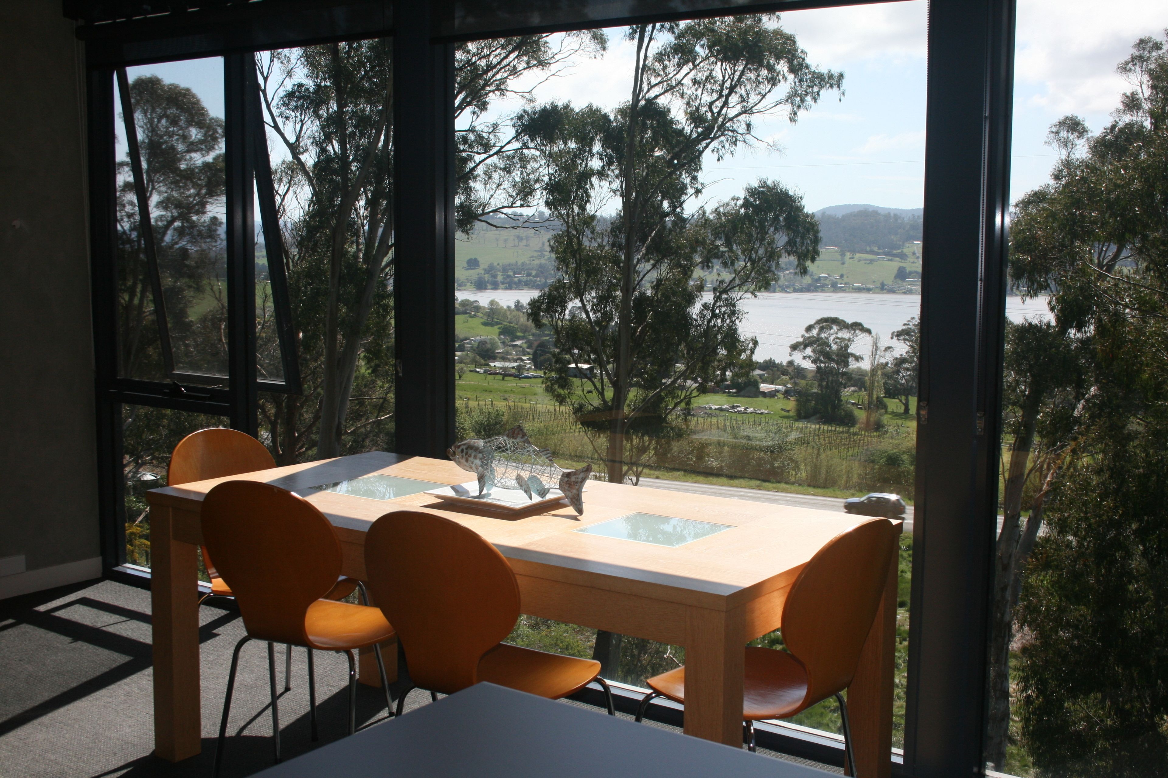 A dining area with a table and chairs, large windows with a view of a lake and trees.