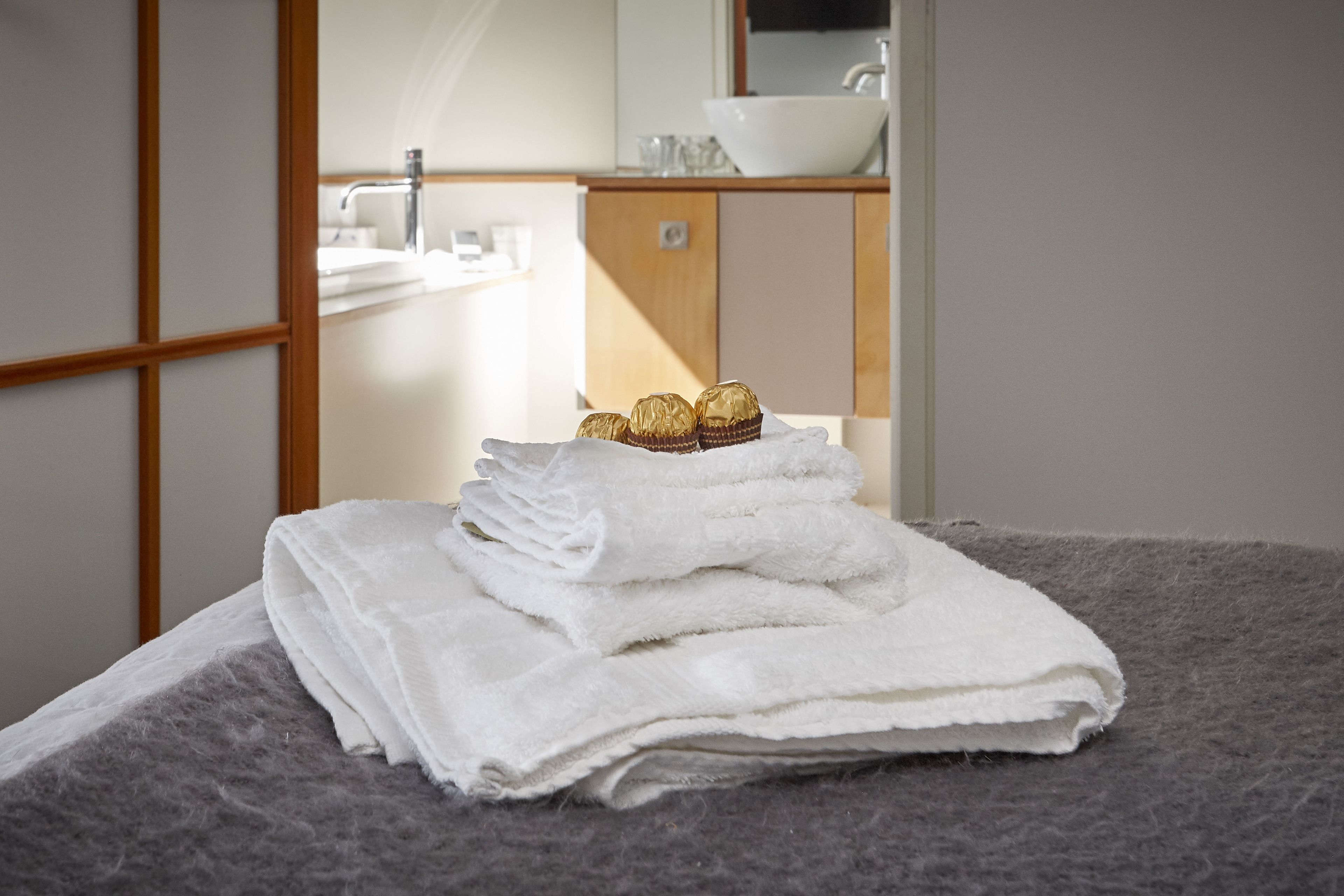 A neatly made bed with white towels and a small stack of chocolates.