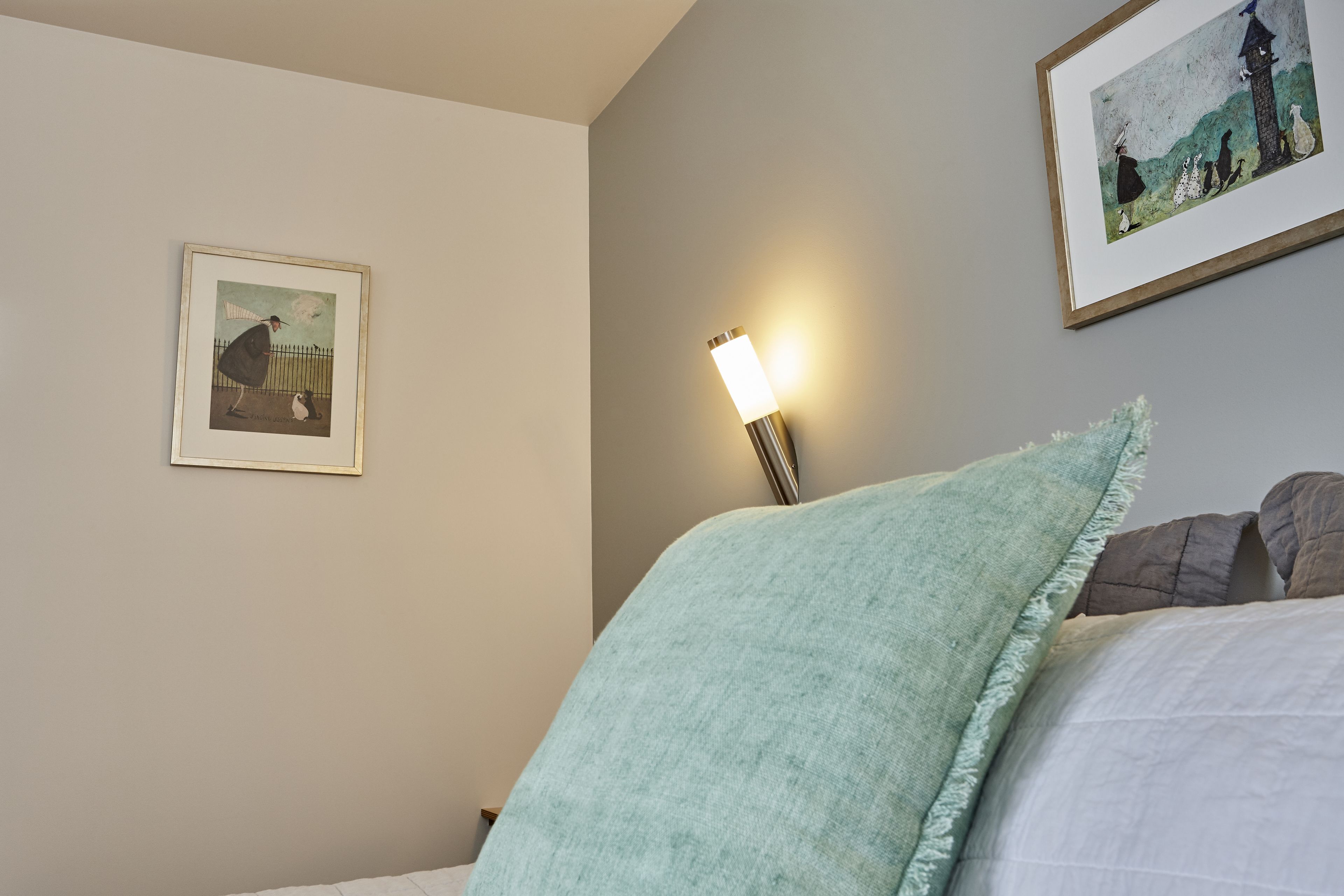 Een slaapkamer met een bed, een nachtkastje, een wandlamp en twee ingelijste foto’s.