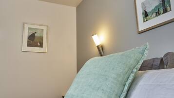 Een slaapkamer met een bed, een nachtkastje, een wandlamp en twee ingelijste foto’s.