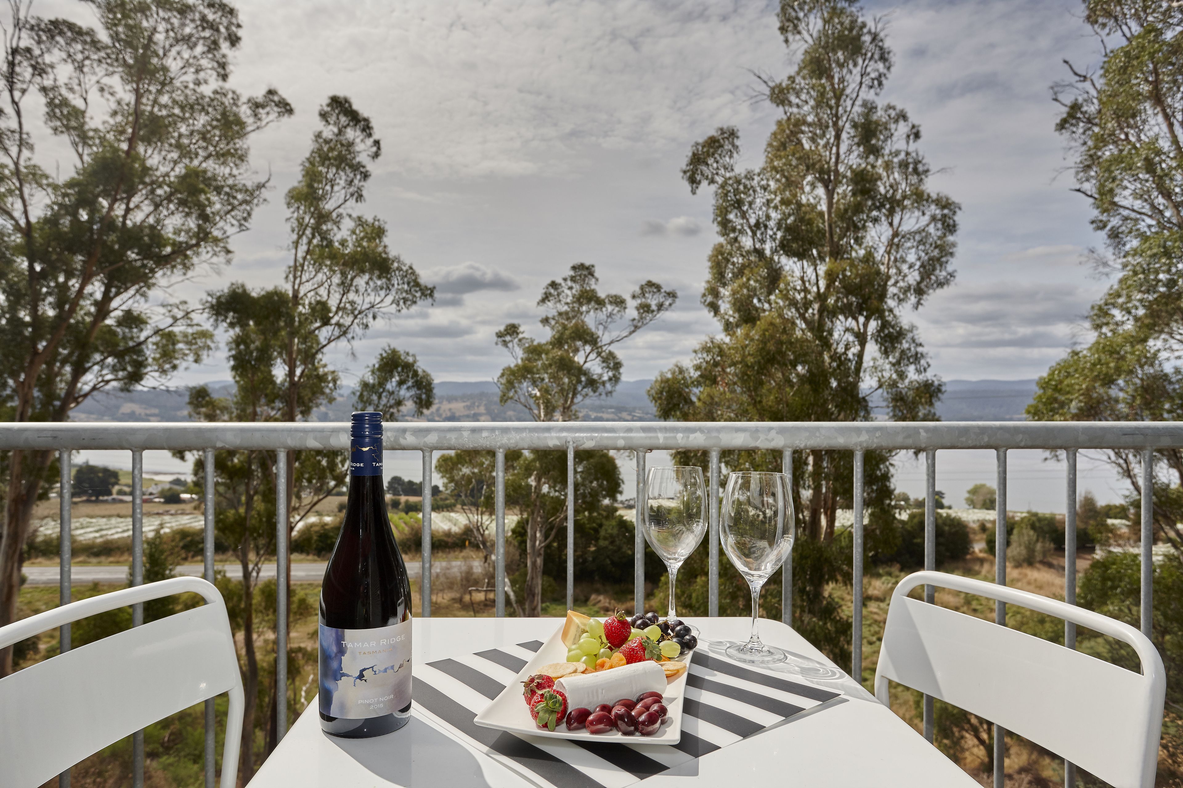Een tafel met een fles wijn, een glas en een fruitschaal op een balkon met uitzicht op een prachtig landschap.