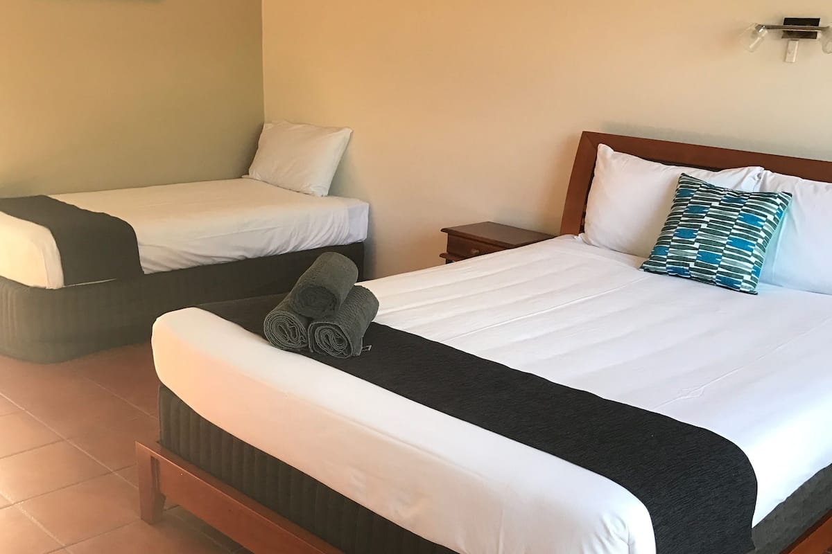 A hotel room with a large bed, a smaller bed, a nightstand, a wall-mounted light, and a framed picture on the wall.
