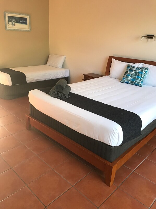 A hotel room with a large bed, a smaller bed, a nightstand, a wall-mounted light, and a framed picture on the wall.