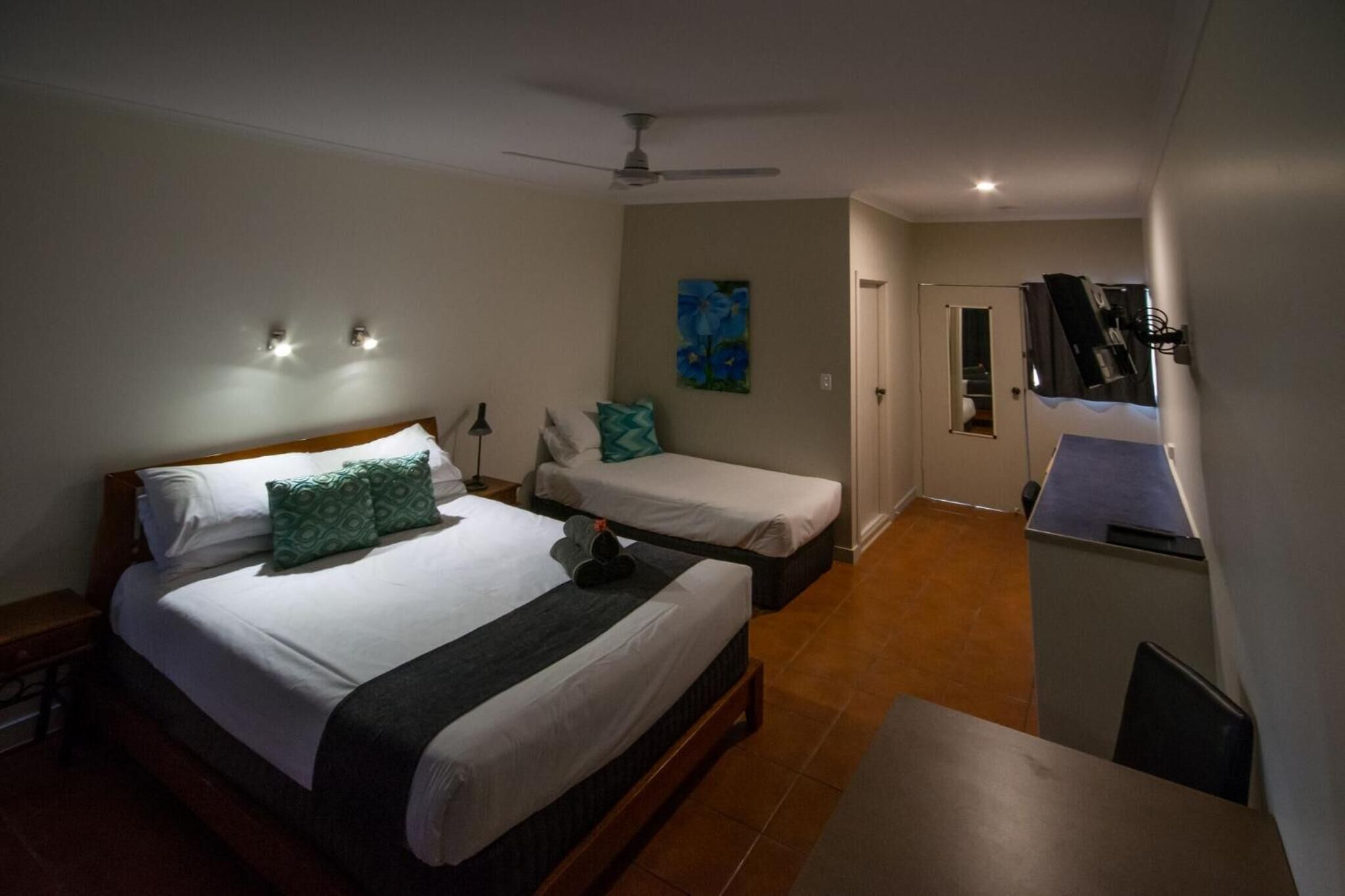 A hotel room with a large bed, two smaller beds, a desk, and a ceiling fan.