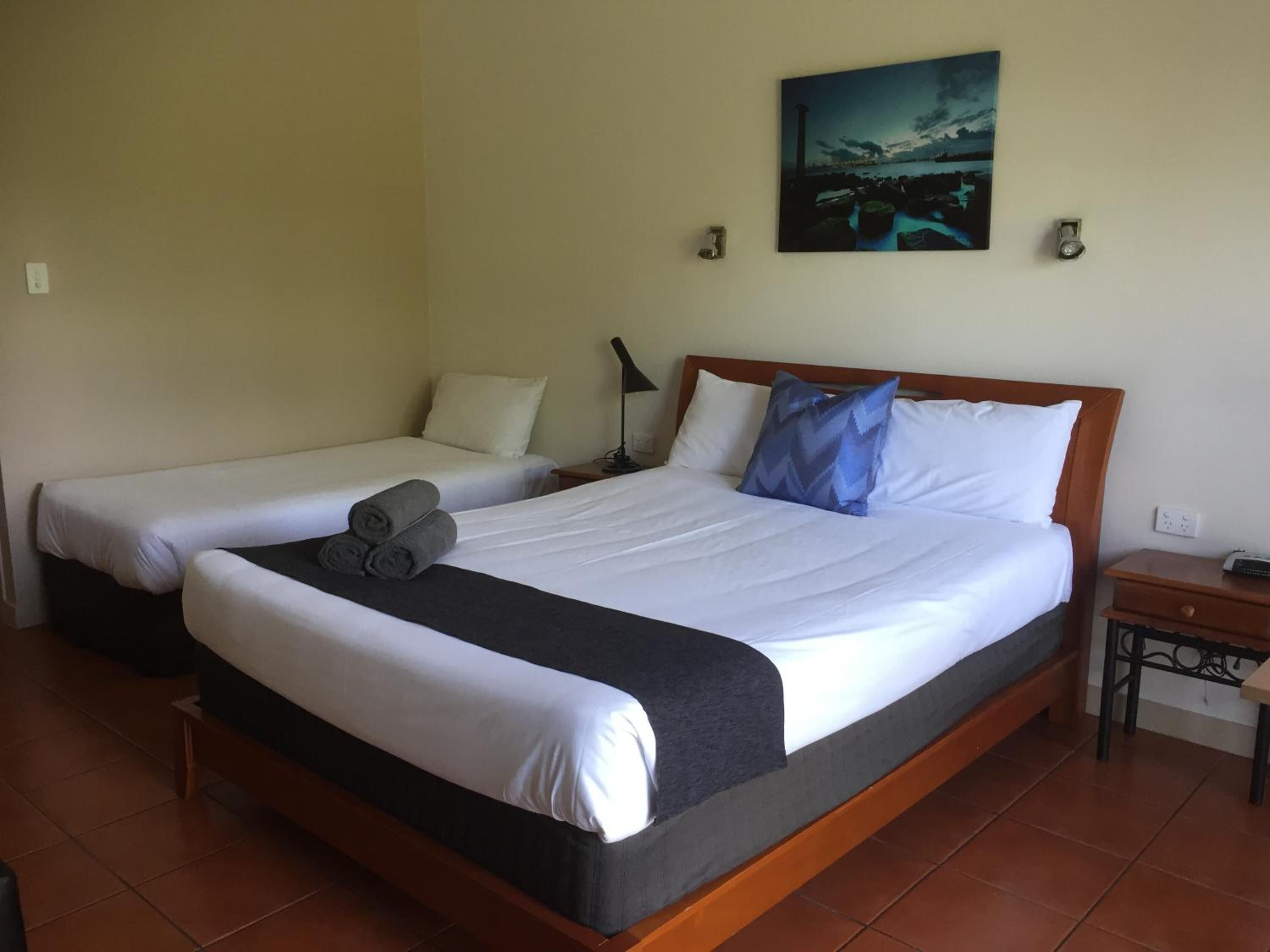 A hotel room with two beds, a nightstand, a lamp, and a painting on the wall.