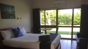 A hotel room with a large bed, a small table, and a view of the outdoors.