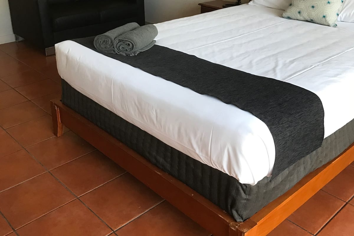 A neatly made bed with white and dark bedding, a black chair, and a small bedside table with a lamp.