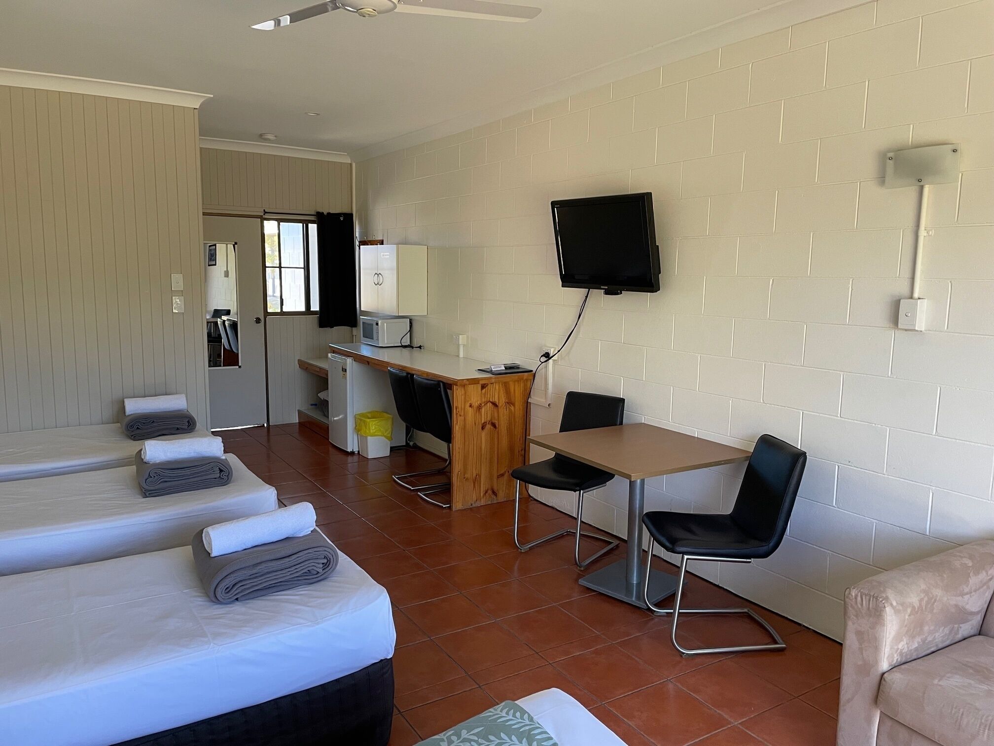 Una habitación de hotel con una cama, un escritorio, una silla, un televisor y una kitchenette pequeña.