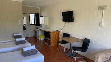 Una habitación de hotel con una cama, un escritorio, una silla, un televisor y una kitchenette pequeña.