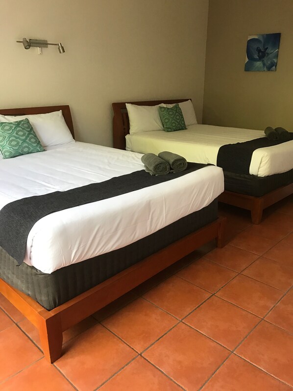 Two single beds with wooden frames, white and black bedding, and green patterned pillows.
